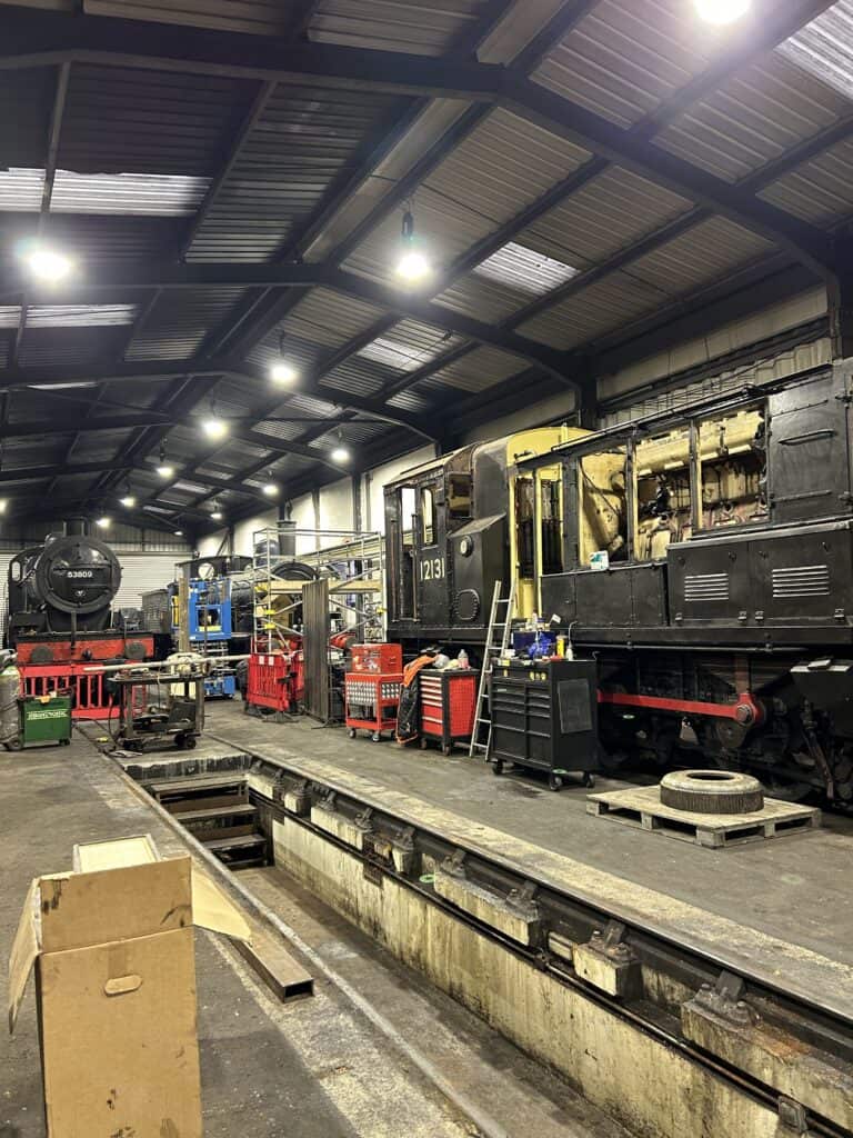 Inside a railway workshop with locomotives and tools.